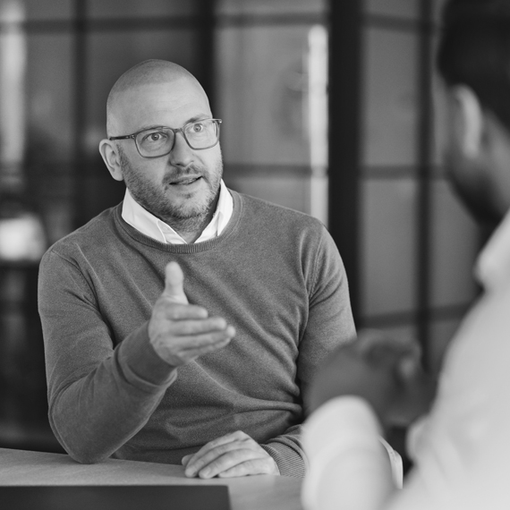 A man wearing glasses talking to his colleague